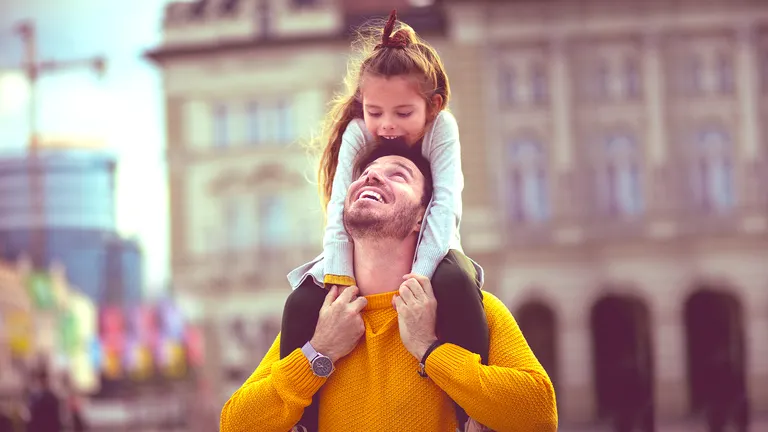 A father and his daughter on his shoulders, both smiling
