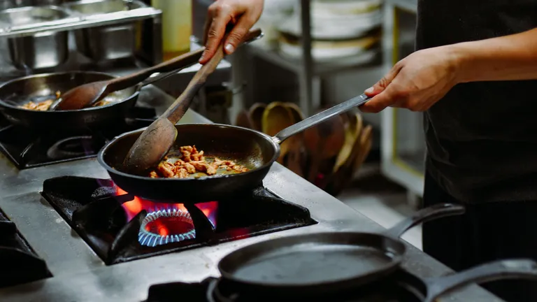 A chef cooking in a pan over a restaurant cooking stove working on natural gas, with flames on